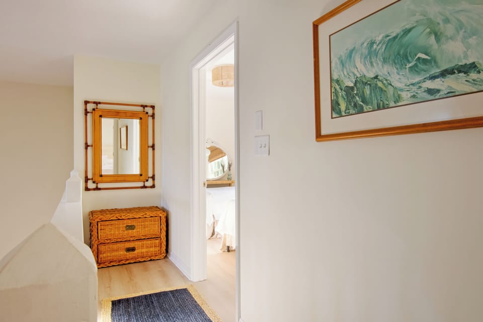 610 Castle Ct - Bright Hallway and Guest Entry - The sun-drenched hallway features light-toned flooring and a classic wood dresser, leading into one of the home's inviting guest bedrooms. Coastal wall art adds a touch of local charm to the crisp white transition space.