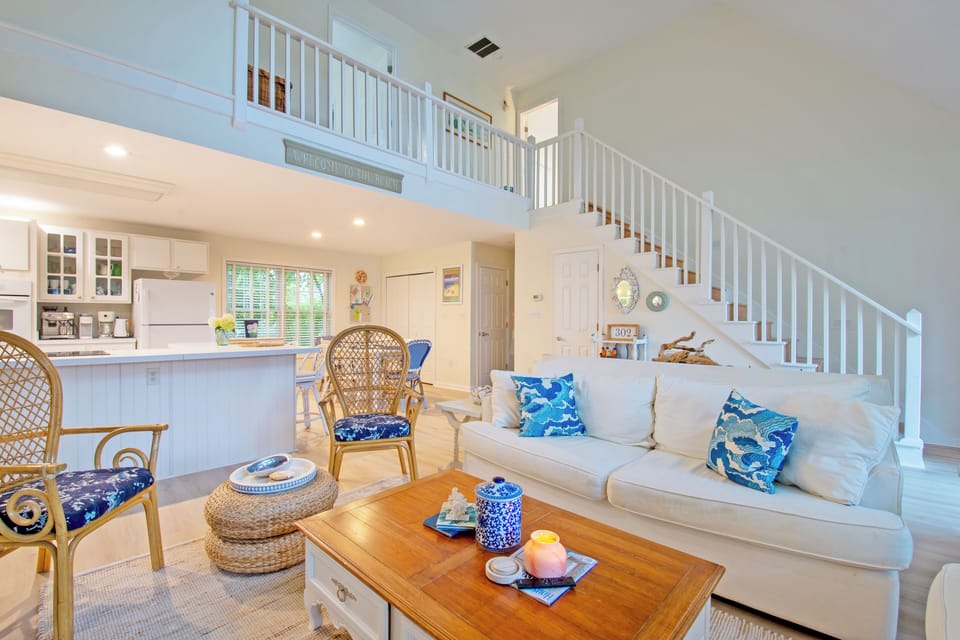 610 Castle Ct - Social Open Floor Plan - The seamless transition from the living area to the kitchen and loft above makes this home ideal for entertaining. A large wooden coffee table and stylish wicker accents add a touch of natural warmth to the contemporary white-on-white interior.