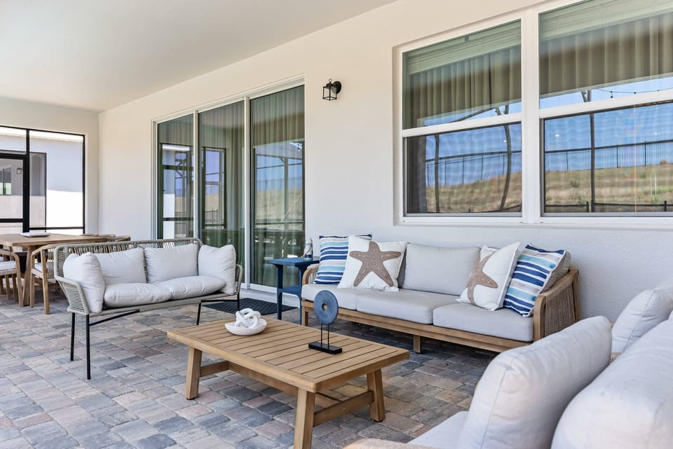 Relax on our spacious patio with cozy neutral and blue cushions, a warm wood coffee table, and bright natural light from large windows, perfect for both gatherings and quiet moments.