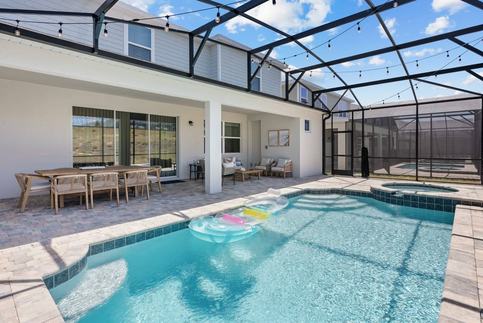 Experience your private oasis with a sparkling pool in a screened enclosure. Delight in al fresco dining at the stylish wooden table, surrounded by sunshine and fresh air, complemented by colorful pool floats for added fun.