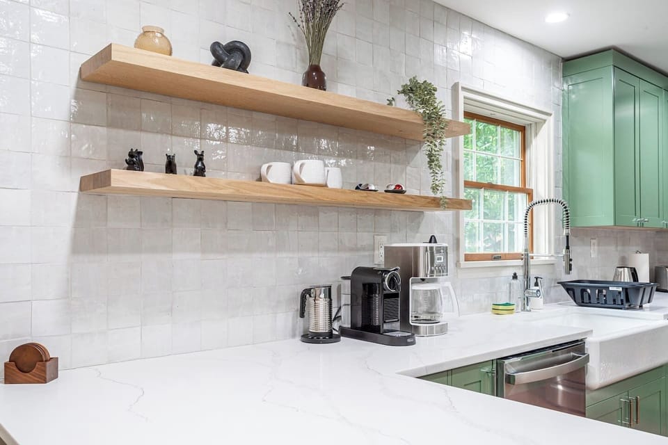 Fully equipped kitchen with sleek white countertops, open shelving, and essential appliances, including a coffee maker. Thoughtfully stocked with all the kitchen essentials and cleaning supplies you need for a comfortable stay.