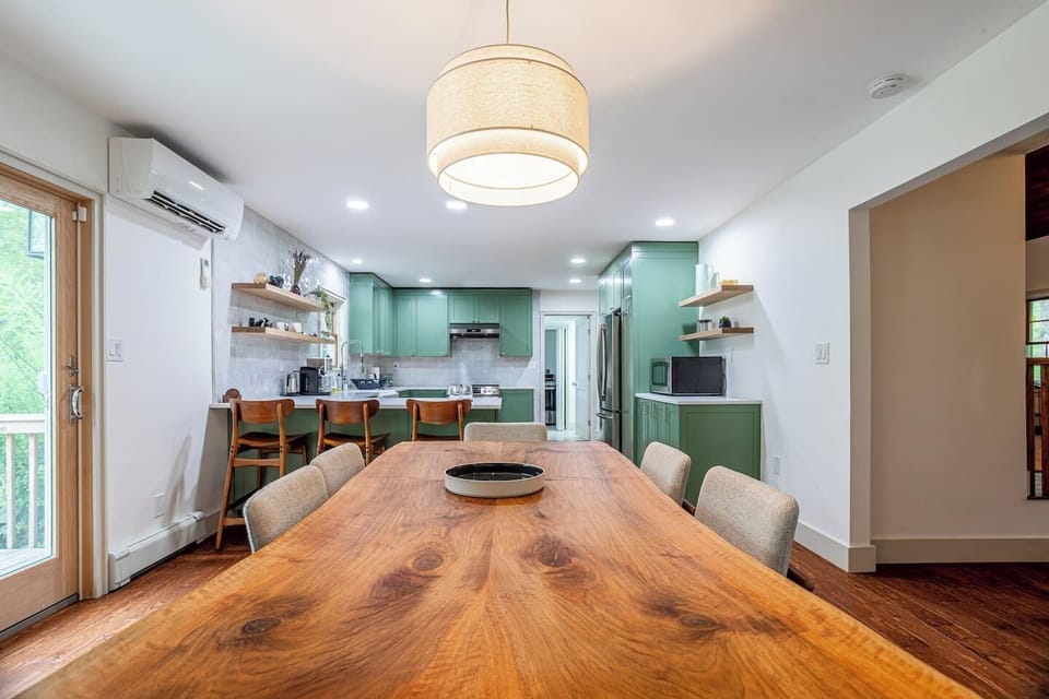 Open-concept dining area leading to a fully equipped kitchen with sage green cabinetry and a cozy breakfast bar. The large wooden table is perfect for gatherings, making this space ideal for both cooking and entertaining.