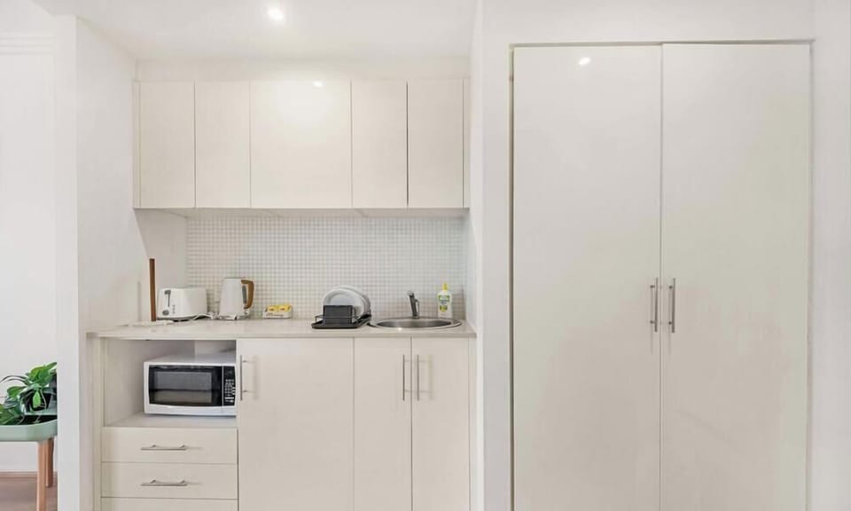 Compact kitchenette with built-in cabinetry, microwave, sink, and storage cupboard.