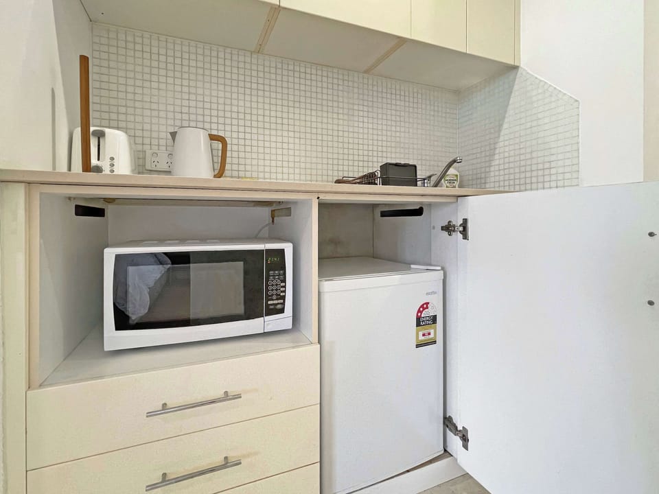 Compact kitchenette with built-in cabinetry, microwave, sink, and storage cupboard.