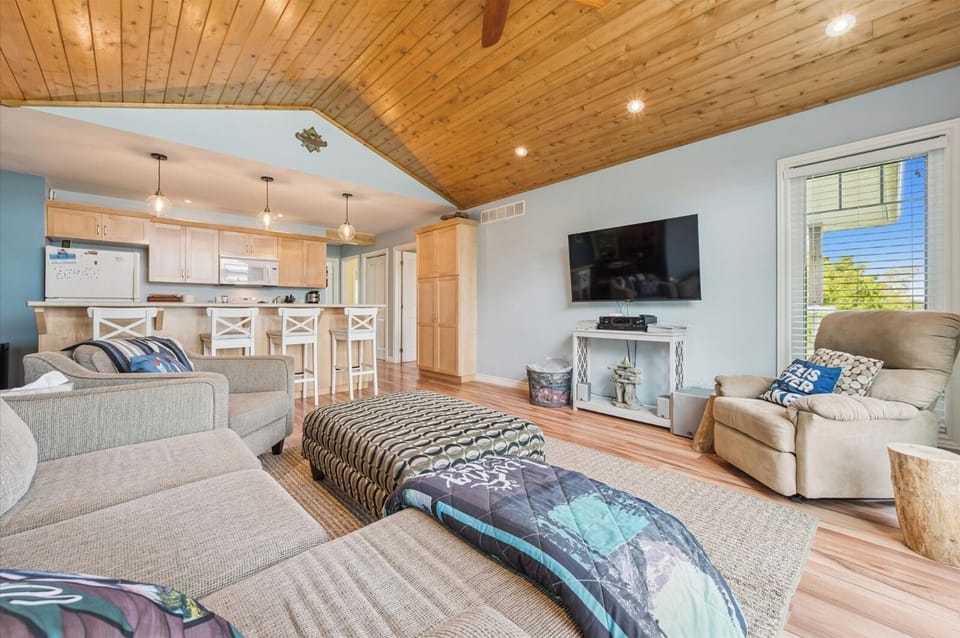 Open-concept living area with cozy seating, vaulted wood ceiling, and a breakfast bar connecting to the kitchen.