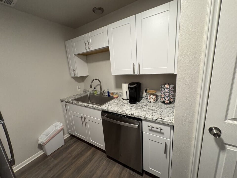 Modern and practical kitchen equipped with large stainless steel sink, dishwasher, Keurig coffee maker, coffee pods, and creamer pods.
