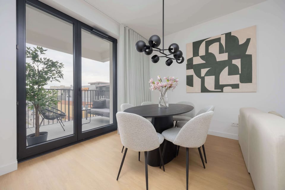 A bright dining area next to a window with a view, decorated with a flower vase on the table.