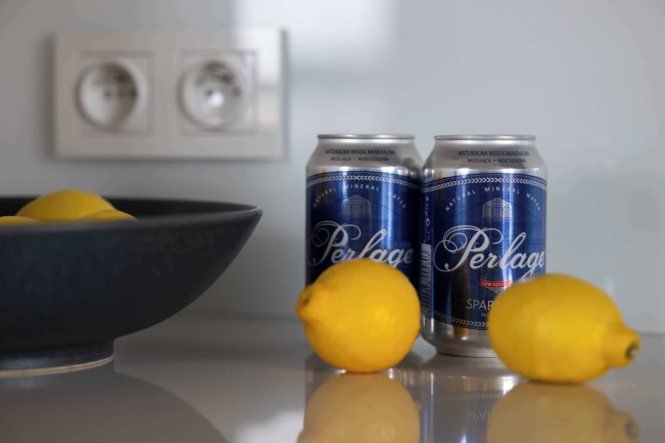 A kitchen counter with a black bowl, lemons, and two cans of soda as decoration.