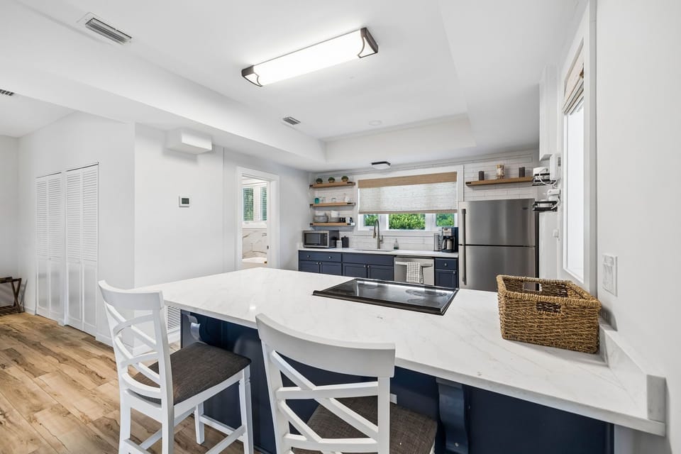 Your modern kitchen awaits with sleek marble counters, navy cabinetry, and stainless steel appliances. Natural light pours in through the window as you gather around the spacious island—perfect for cooking or catching up.