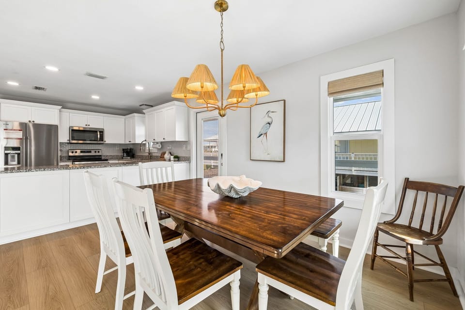 Gather around the rich wood dining table beneath warm chandelier light. Your open kitchen flows seamlessly into this inviting space, perfect for morning coffee or evening meals together.