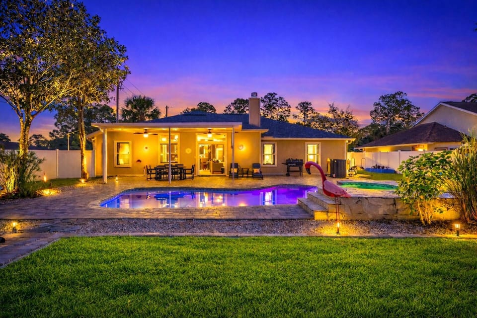A glowing pool at night with vibrant LED colors reflecting on the water, set against a stunning sunset sky of pinks, blues, and orange.