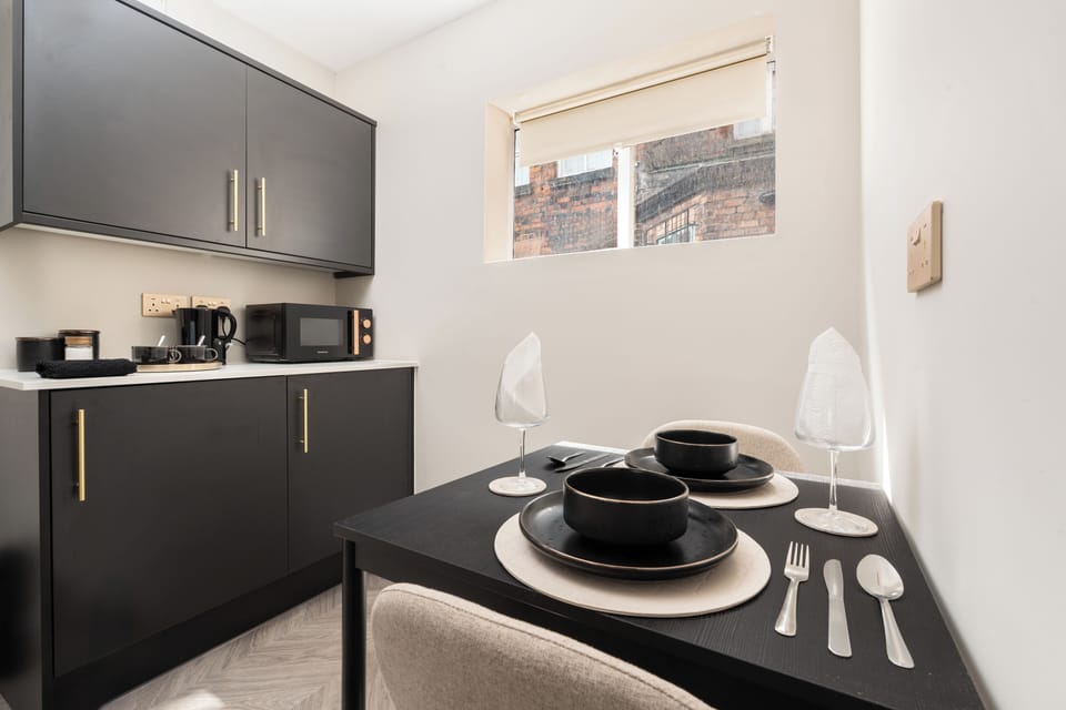Compact yet practical, the kitchenette includes a two-seater dining space, microwave, toaster, kettle, fridge, and all essentials like tea, coffee, sugar, glasses, and cutlery. A wardrobe, wall mirror, iron, hairdryer, and board add extra convenience