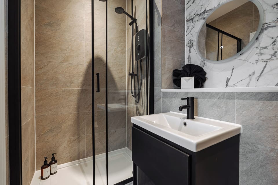 A clean, modern bathroom with an electric shower, toilet, sink, and small makeup mirror—providing everything you need to refresh and prepare for the day ahead.