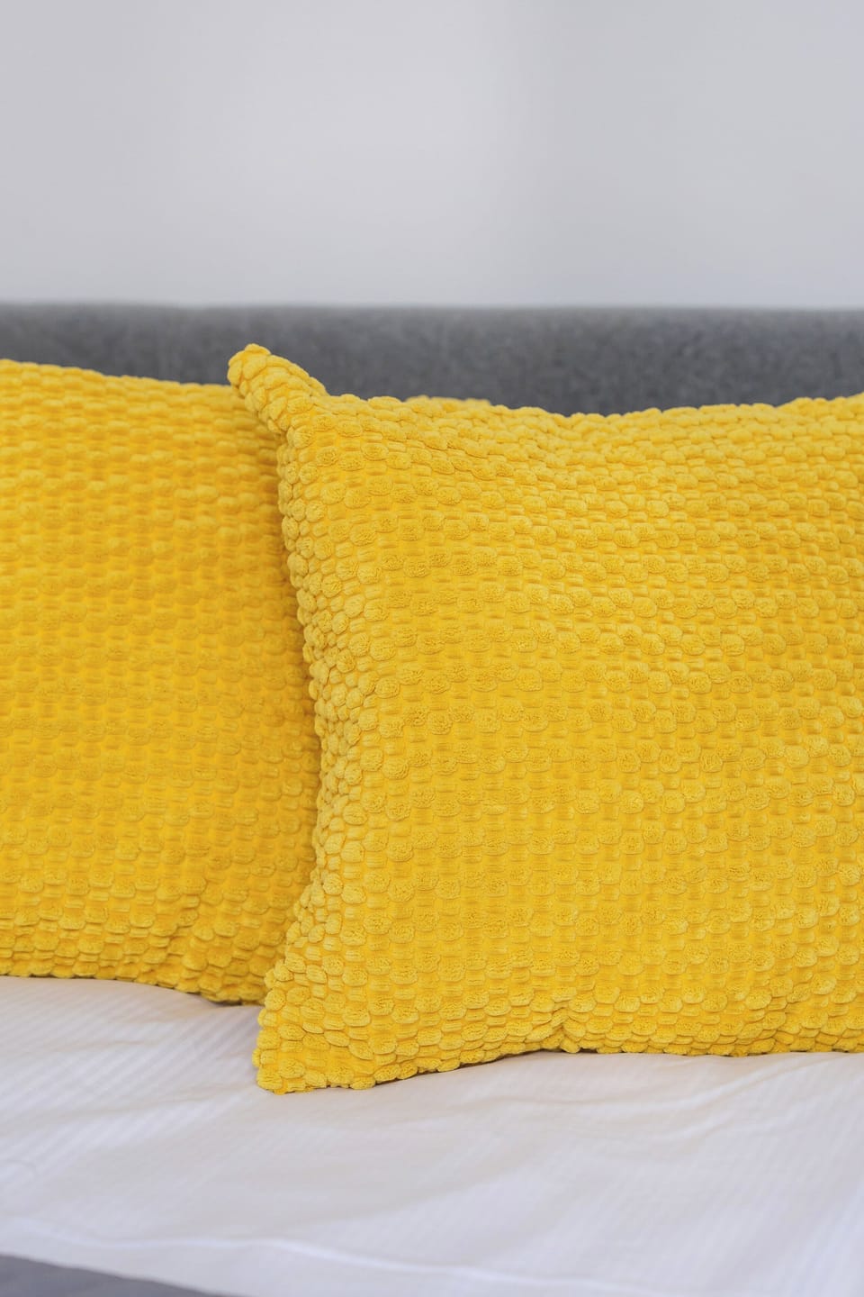 A close-up of a bed with bright yellow pillows against a gray bedspread. The vibrant color adds warmth to the room.