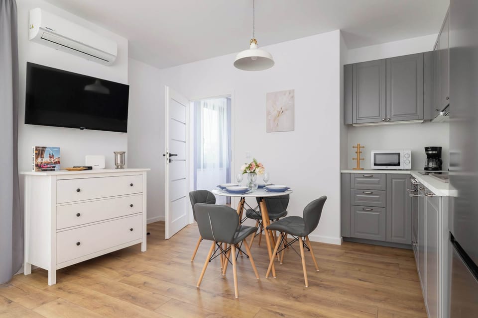 A compact dining area with a round table and modern chairs next to a wall-mounted TV. The kitchen area is conveniently located nearby.