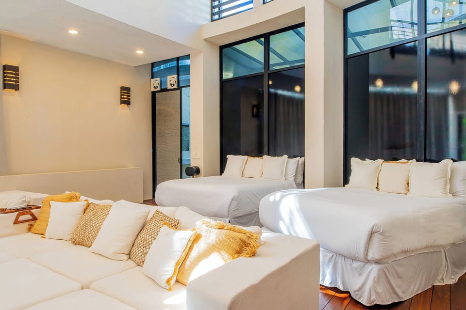 Your modern bedroom features two comfortable beds with crisp white linens and golden accents, flooded with natural light from floor-to-ceiling windows.