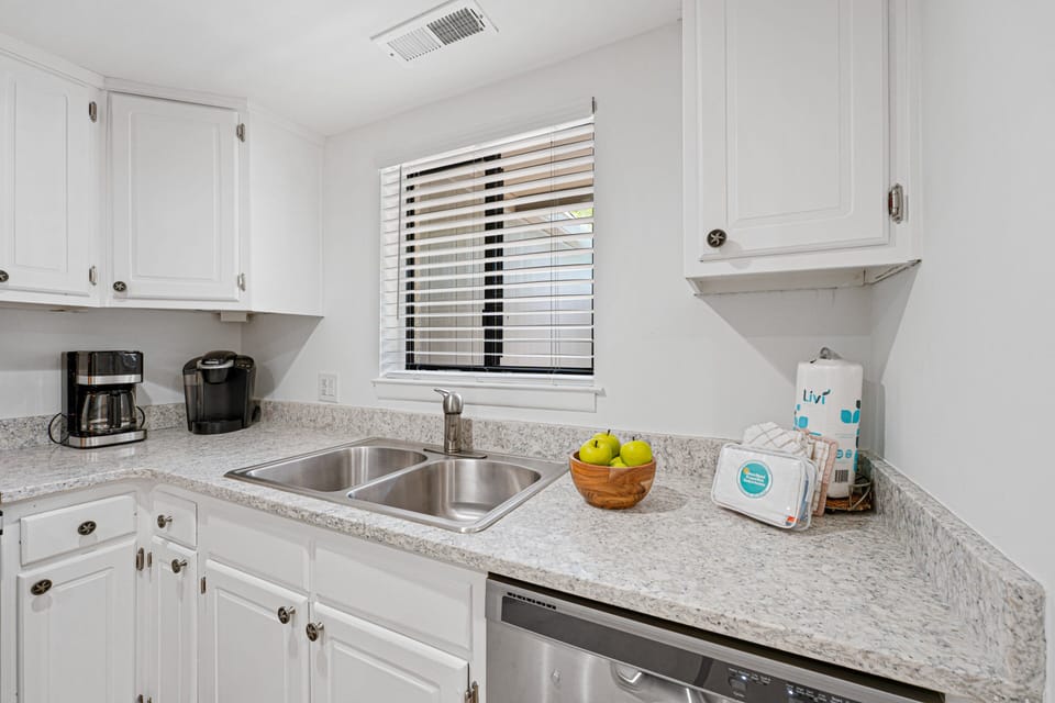 Granite-style countertops, a double-basin sink, stainless steel dishwasher, and dedicated coffee station provide everything needed for a comfortable stay