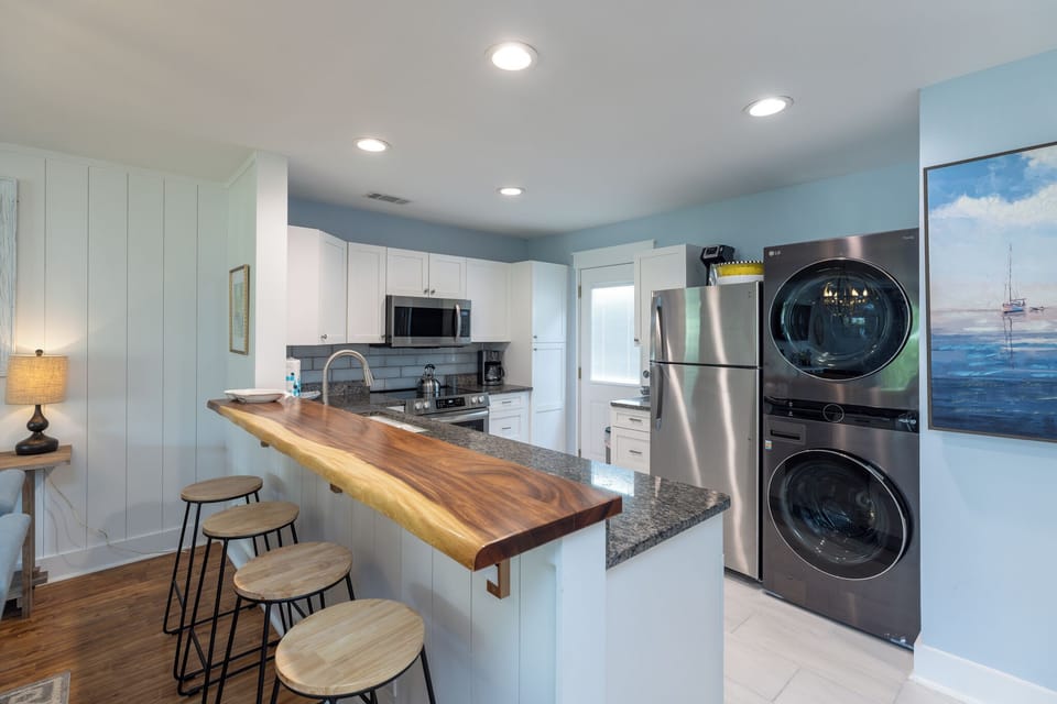 Modern coastal kitchen with white cabinetry, stainless steel appliances, and a natural wood breakfast bar.