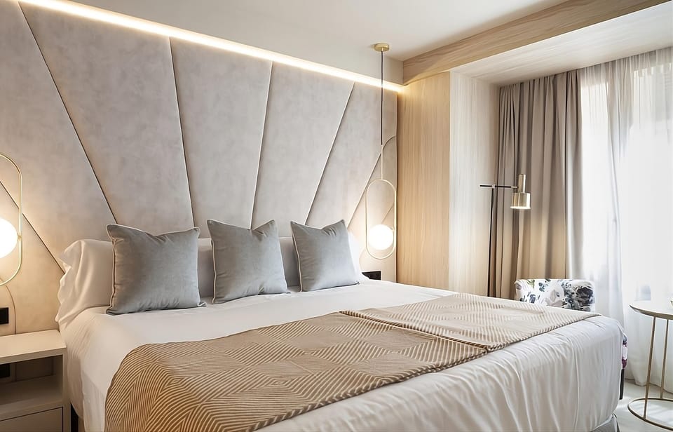 Unwind in plush bedding beneath soft lighting and sheer curtains.