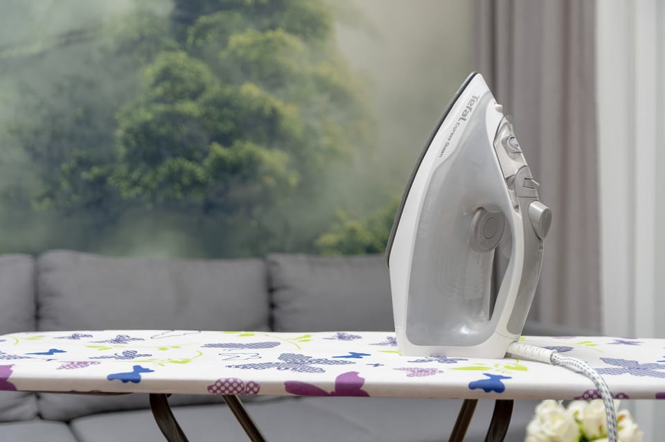An ironing board by the window with a view of greenery provides a convenient spot for preparing clothes before going out.