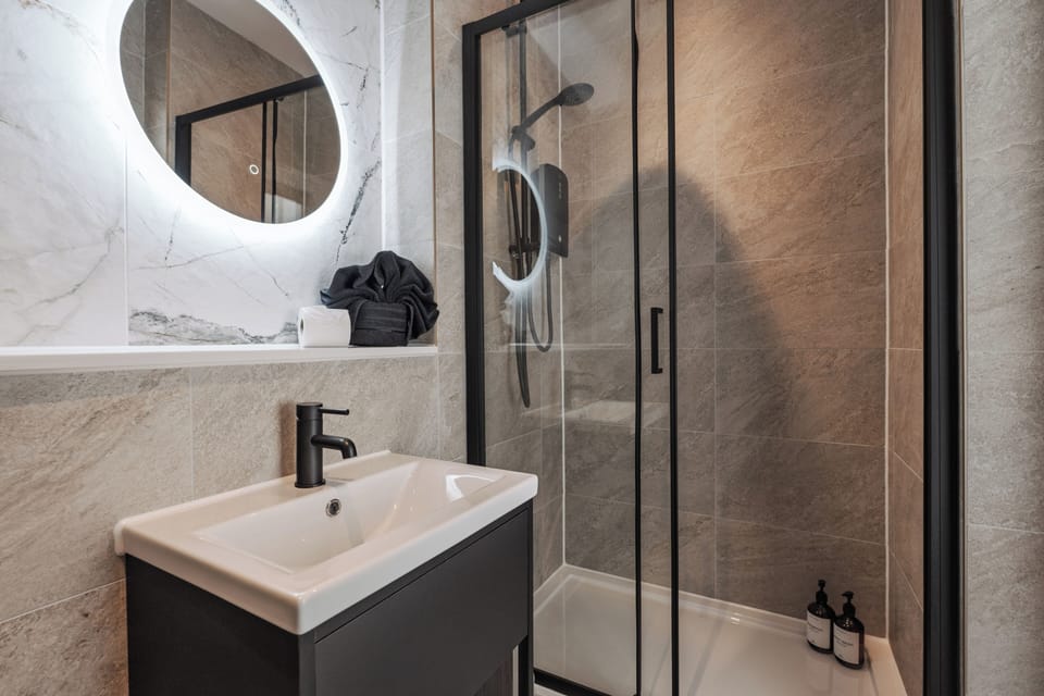 A clean, modern bathroom with an electric shower, toilet, sink, and small makeup mirror—providing everything you need to refresh and prepare for the day ahead.