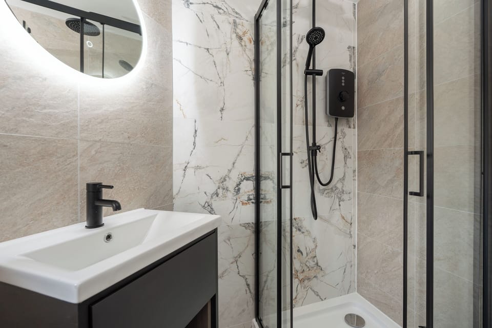 A clean, modern bathroom with an electric shower, toilet, sink, and small makeup mirror—providing everything you need to refresh and prepare for the day ahead.