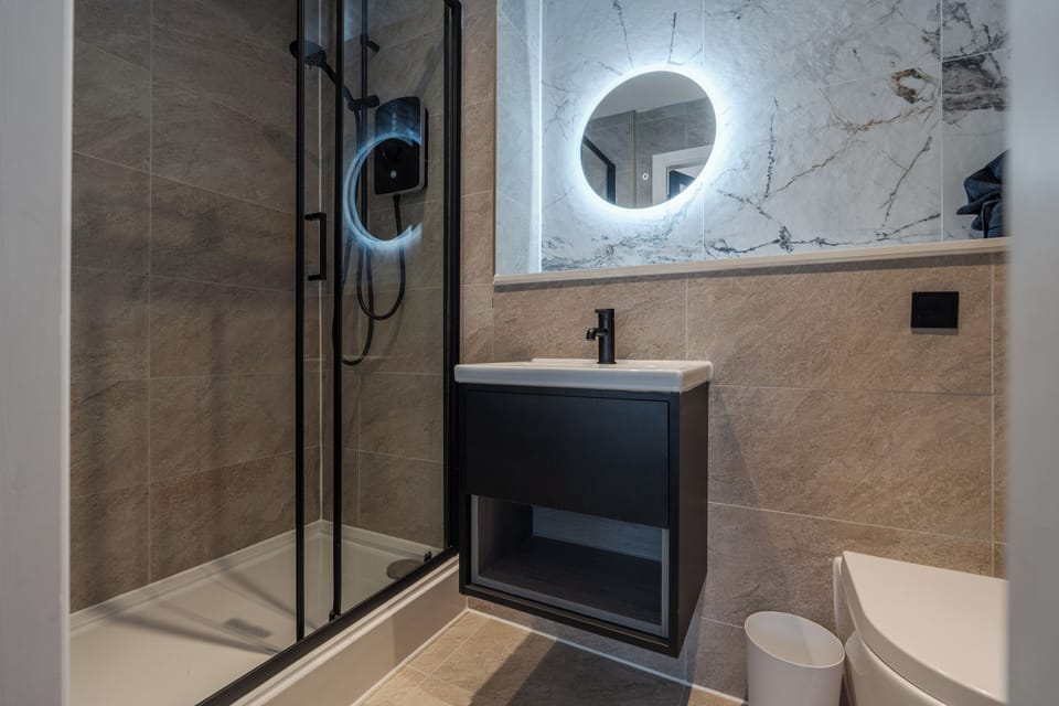 A clean, modern bathroom with an electric shower, toilet, sink, and small makeup mirror—providing everything you need to refresh and prepare for the day ahead.
