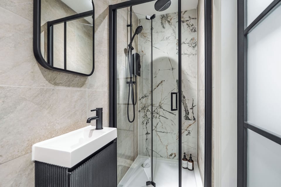 A clean, modern bathroom with an electric shower, toilet, sink, and small makeup mirror—providing everything you need to refresh and prepare for the day ahead.