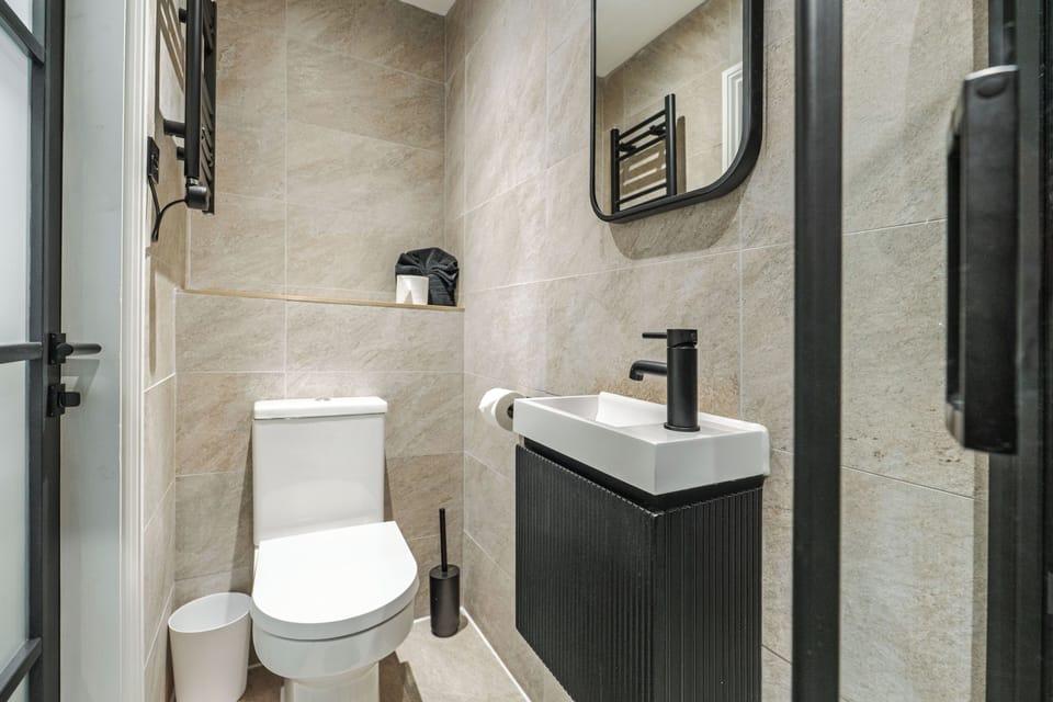 A clean, modern bathroom with an electric shower, toilet, sink, and small makeup mirror—providing everything you need to refresh and prepare for the day ahead.