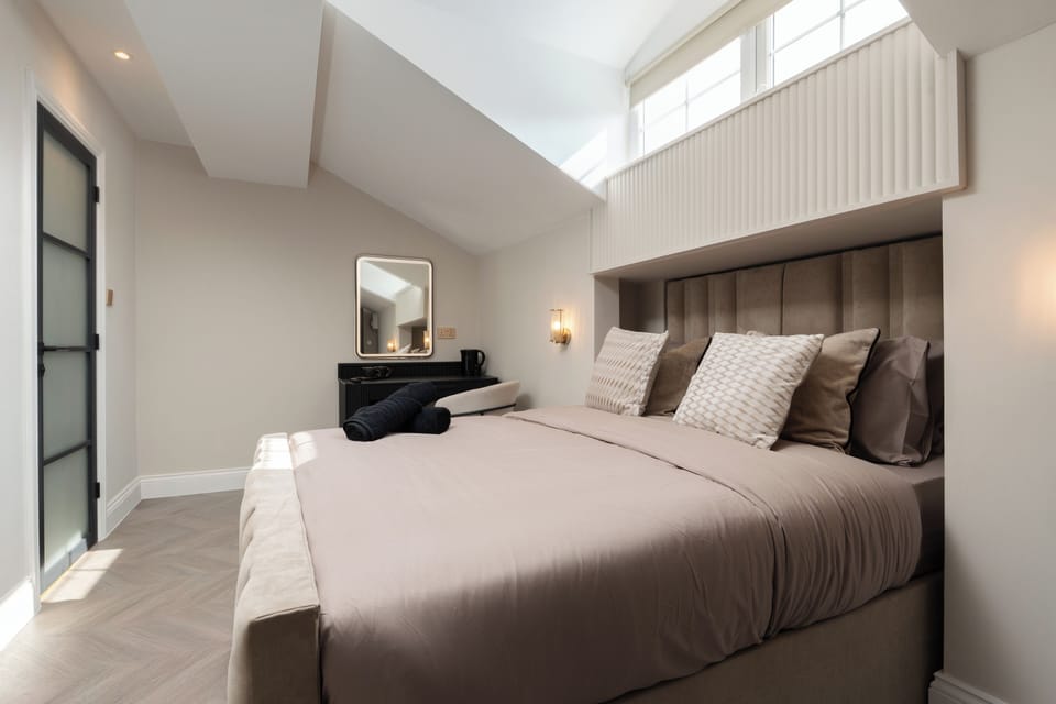A bright, open-plan studio featuring a king bed, Smart TV with Netflix, a wardrobe, a cosy fireplace, and a dressing table that doubles as a vanity and work desk—ideal for relaxing, working, or getting ready for the day.
