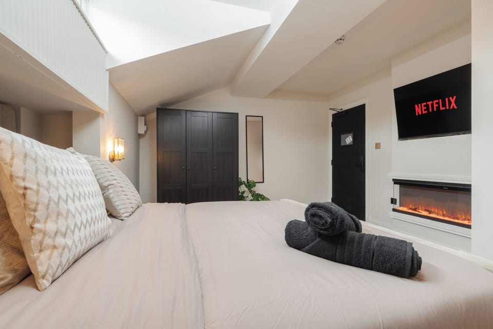 A bright, open-plan studio featuring a king bed, Smart TV with Netflix, a wardrobe, a cosy fireplace, and a dressing table that doubles as a vanity and work desk—ideal for relaxing, working, or getting ready for the day.
