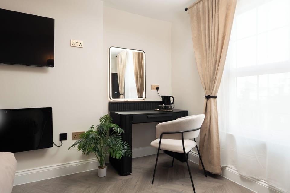 A bright, open-plan space featuring a comfortable double bed, vanity unit with mirror, wardrobe, Smart TV, and electric heater—perfect for relaxing or getting ready for a night out in the city.
