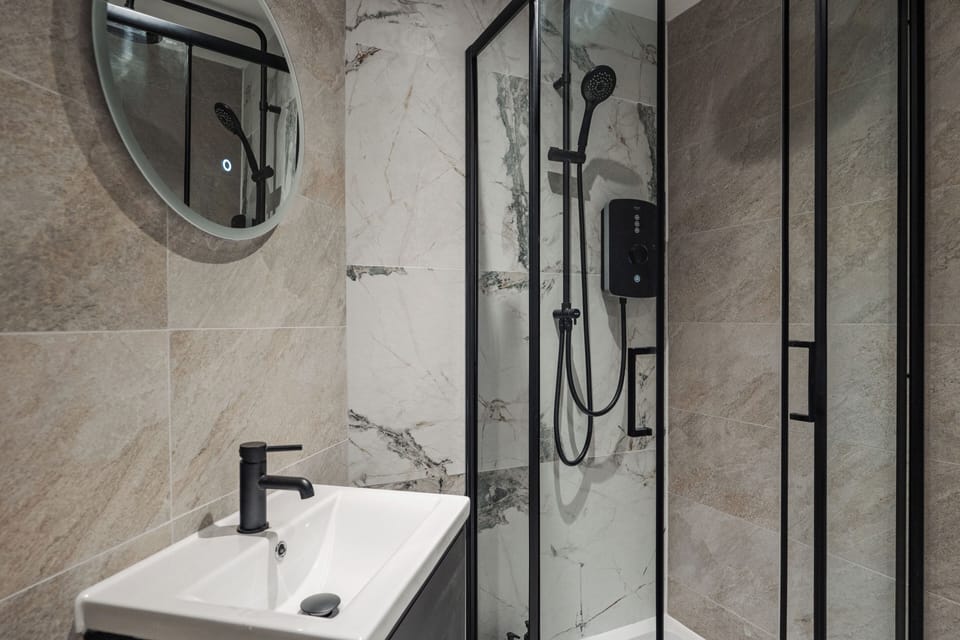 A clean, modern bathroom with an electric shower, toilet, sink, and small makeup mirror—providing everything you need to refresh and prepare for the day ahead.