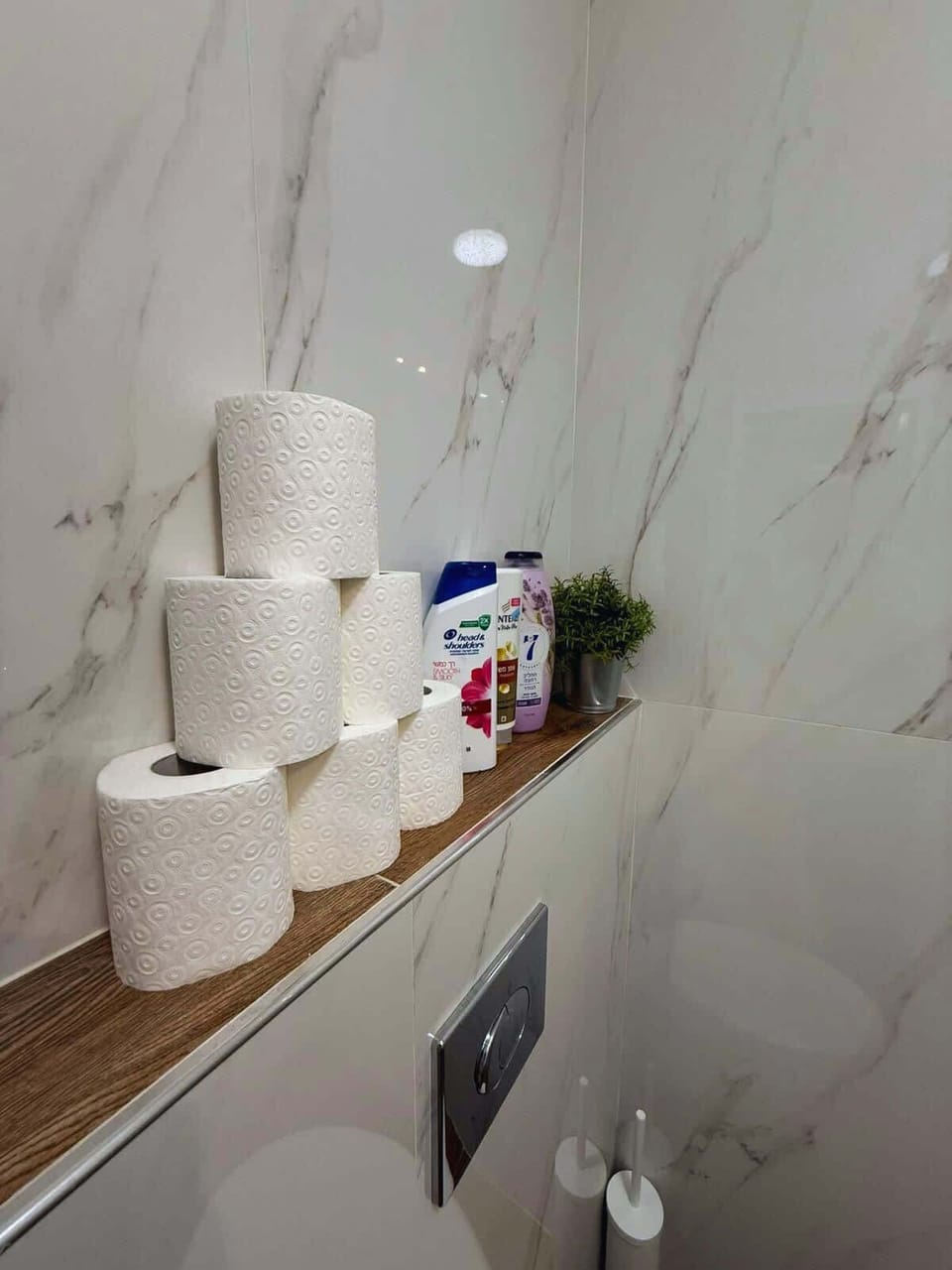 Modern bathroom with glass walk-in shower, rainfall showerhead, marble style walls, wood look flooring, and all essentials provided for a comfortable stay.