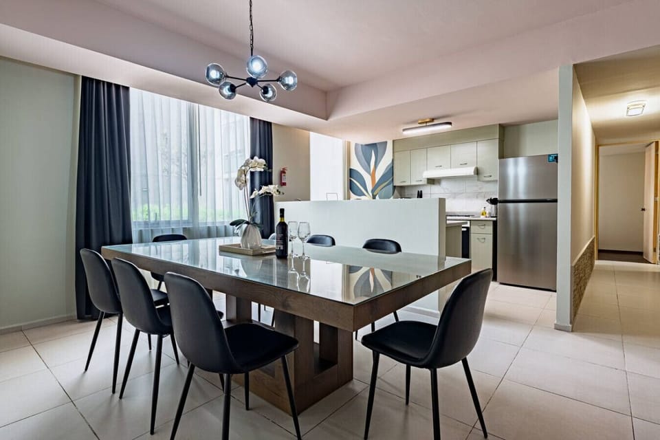 A well-lit dining area with a wooden table, dark chairs, and a view into an adjacent room