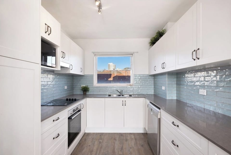 kitchen layout featuring glossy white cabinetry, a stylish grey tiled backsplash, and modern stainless steel appliances