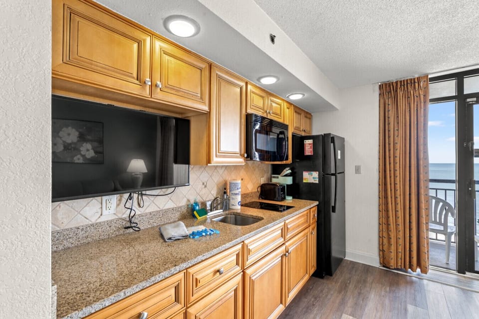 Kitchenette with full-size refrigerator, two stovetop burners, microwave, smart TV, silverware, cookware, and dinnerware. Ideal for preparing vacation snacks or meals during your Myrtle Beach beach getaway.