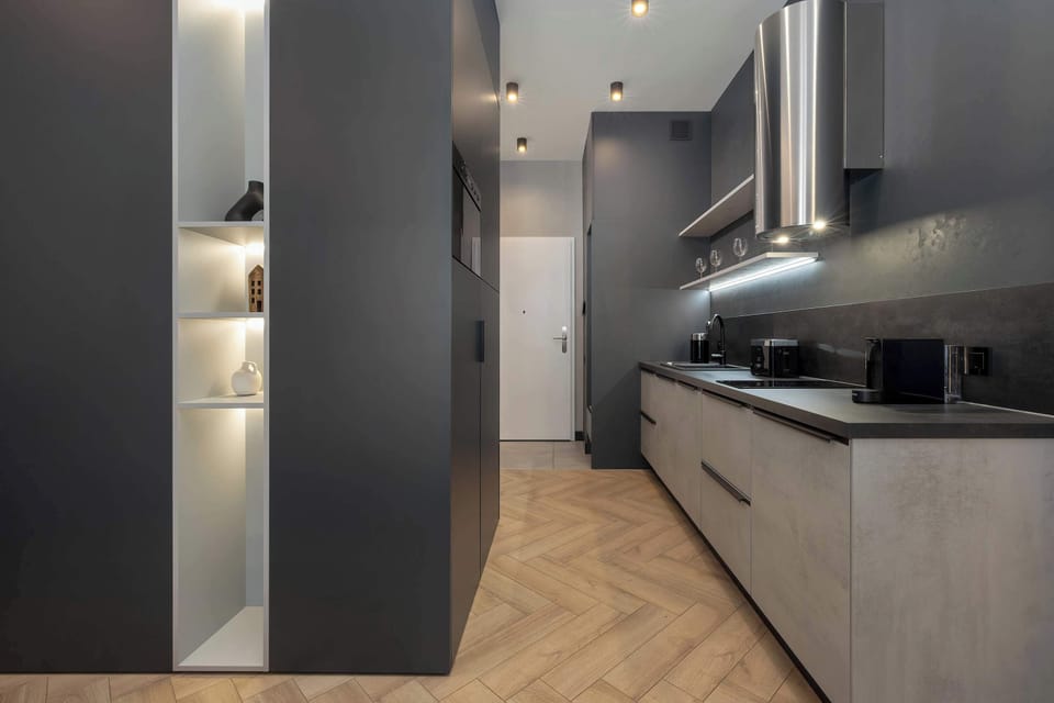 A hallway leading into a kitchen, with dark cabinetry and elegant design. Subtle lighting gives the space a cozy feel.