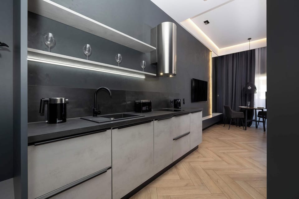 A contemporary kitchen space with smooth gray surfaces and ambient LED lighting. The open layout leads into the living area.