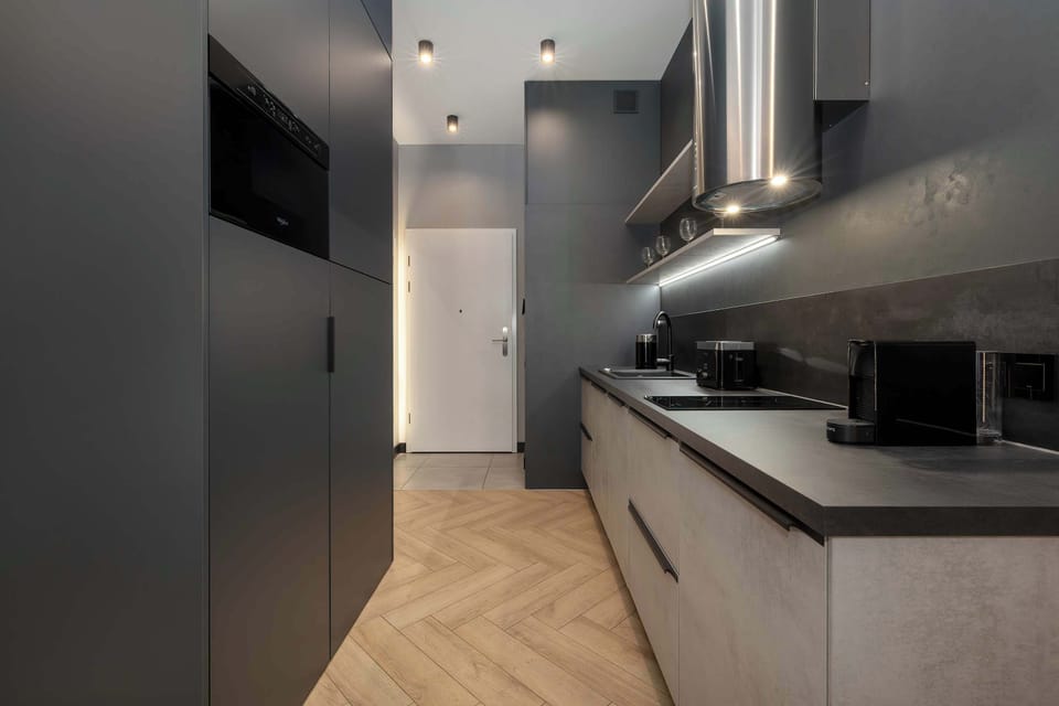 A sleek kitchenette with dark cabinetry, integrated appliances, and under-cabinet lighting. The design maximizes storage in a compact space.