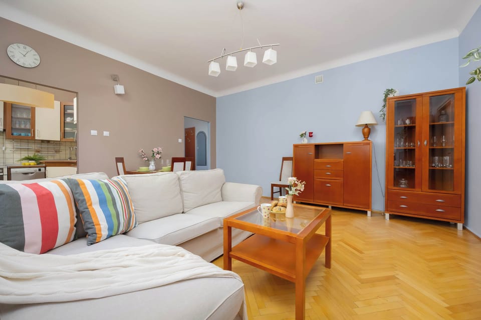 A bright living room with wooden flooring, a table, chairs, and a large window letting in natural light.
