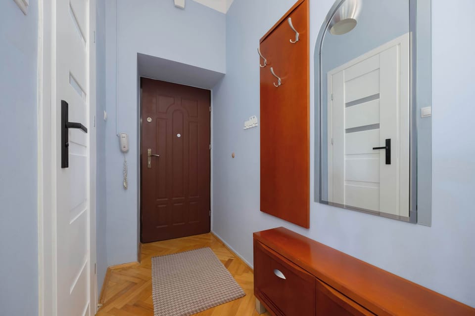 A hallway with a wooden floor, large mirror, and entrance door.