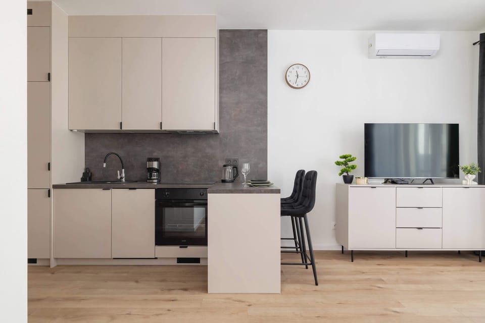 A clean and minimalist kitchen with white cabinetry, a black sink, and a stovetop.