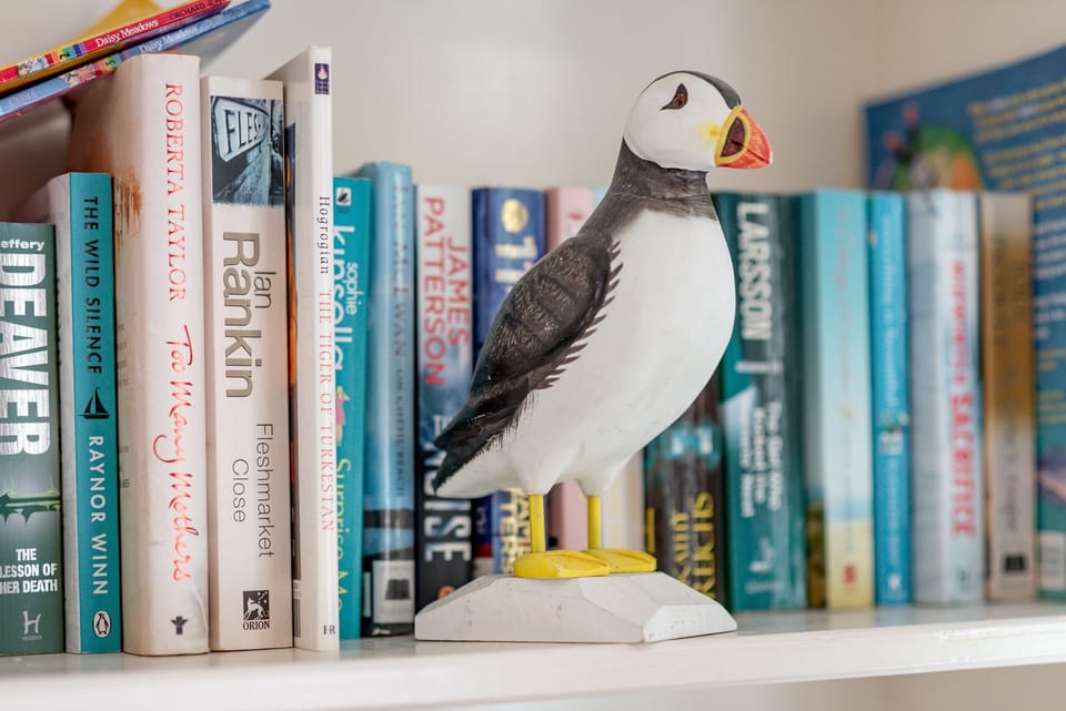 Bookshelf with coastal titles and puffin ornament in the lounge at Earls Lodge, Earlsferry.