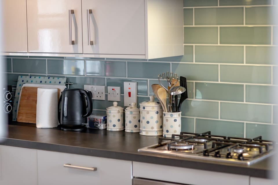 Sleek kitchen with gas hob, glossy cabinets and green subway tiles at Earls Lodge holiday home.