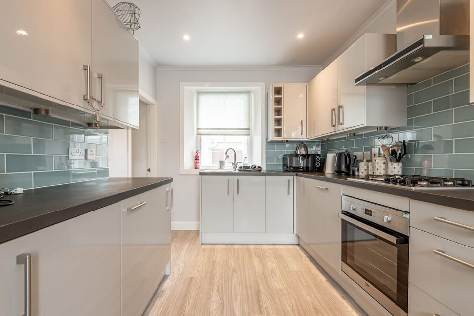 Glossy cabinets, wood-look floor and green subway splashback in the modern kitchen at Earls Lodge.