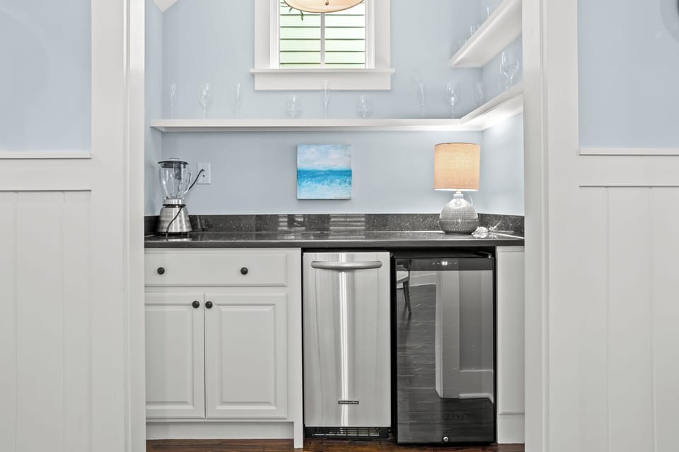 Compact beverage station w/ granite counter, sink & glass-front fridge for easy snacks and drinks.