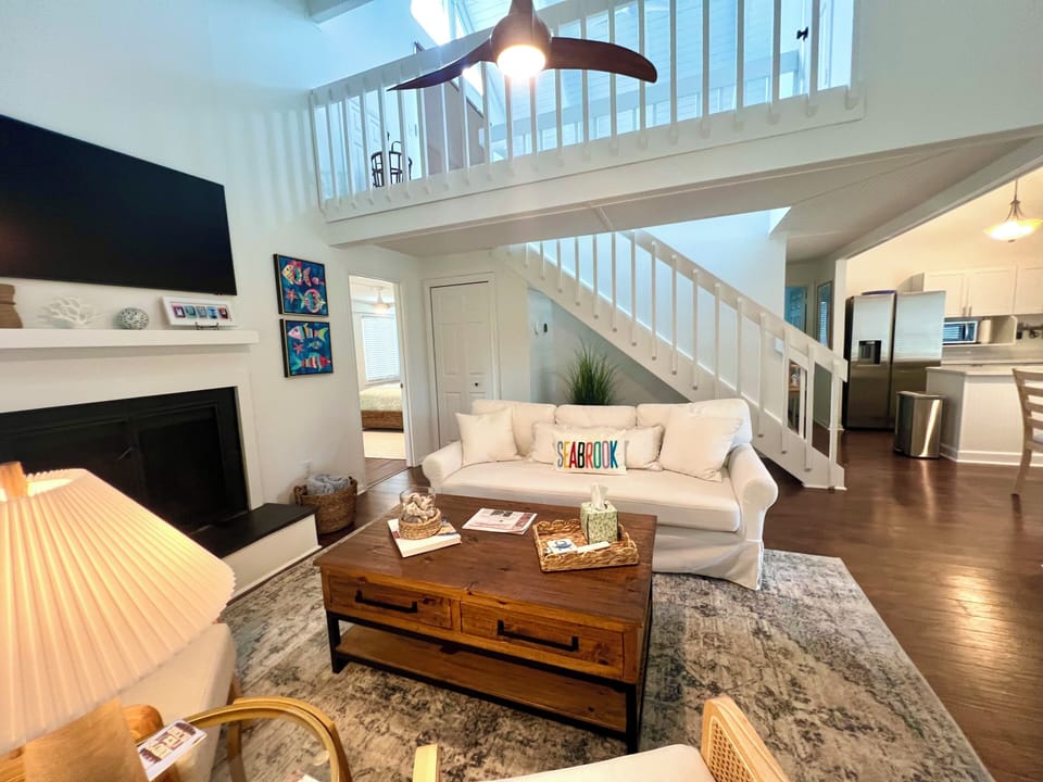 The spacious open living area features a fireplace, vaulted ceiling, and staircase leading to the loft, creating an airy coastal retreat.