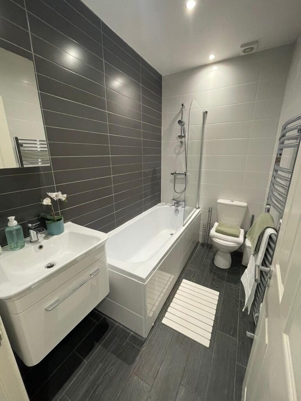 A full bathroom with a sink, toilet, and electric shower over bath, offering a clean and practical space to refresh. Fresh towels are provided for your stay.
