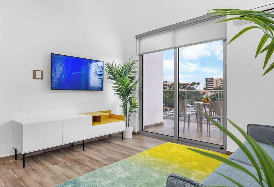 Bright living room with a TV and a balcony offering a refreshing outdoor view.